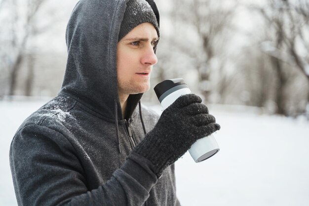 Athlète de jeune homme buvant de la tasse thermique pendant la journée d'hiver enneigée