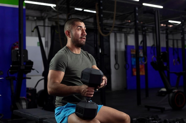 Athlète latin assis sur un banc avec un haltère sur ses jambes pour faire de l'exercice