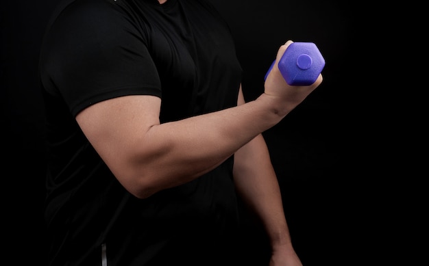 Athlète masculin adulte dans un uniforme noir détient des haltères bleus en plastique violet dans les mains