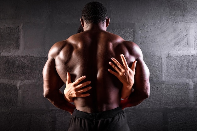 Athlète masculin afro-américain posant démontrant le développement musculaire avec les mains d'une fille sur le dos