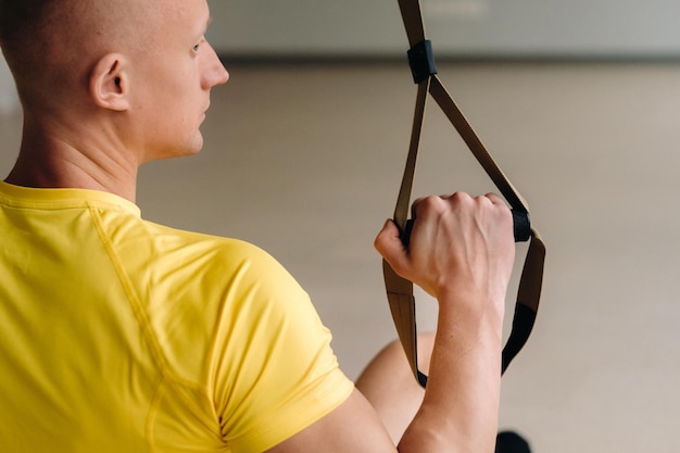 Un athlète masculin concentré effectuant un exercice sur des boucles fonctionnelles dans la salle de sport.