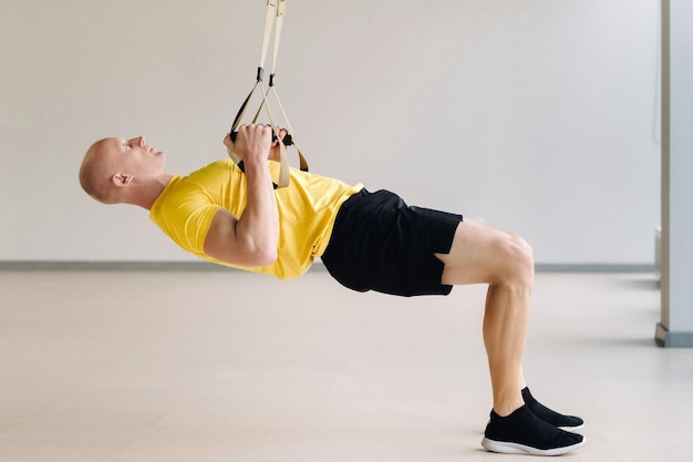 Un athlète masculin concentré effectuant un exercice sur des boucles fonctionnelles dans la salle de sport