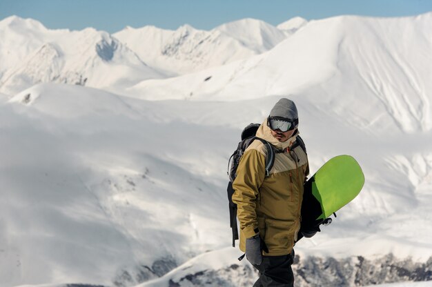 Athlète masculin dans des lunettes de ski de protection, avec un snowboard dans ses mains, monte à la piste