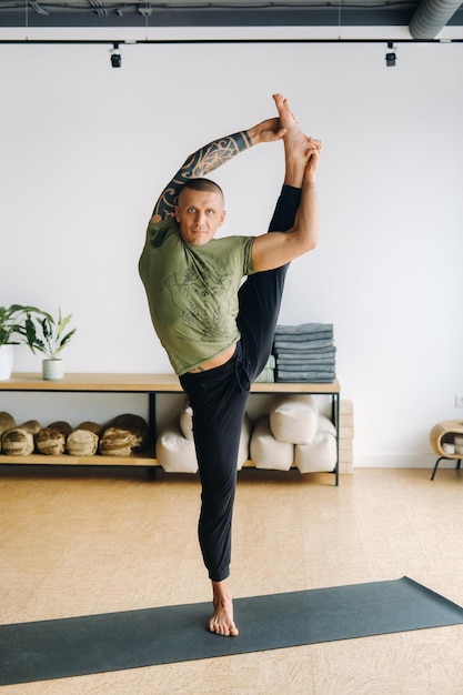 Un athlète masculin dans un t-shirt vert fait du yoga dans la salle de sport