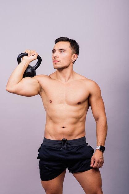 Athlète masculin hispanique travaillant avec kettlebell sur fond gris thème d'entraînement crossfit