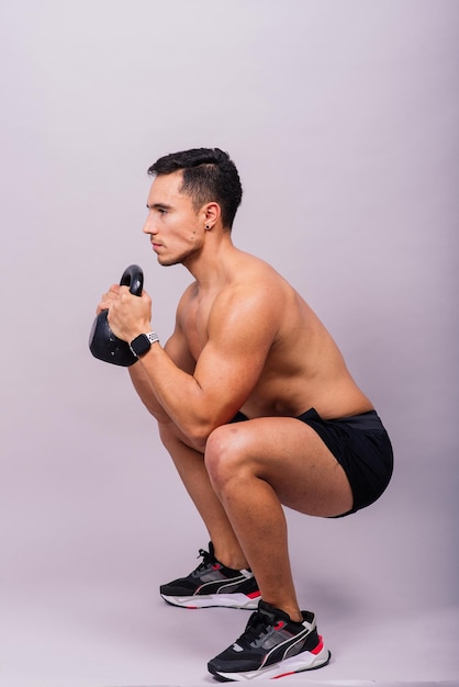 Athlète masculin hispanique travaillant avec kettlebell sur fond gris thème d'entraînement crossfit