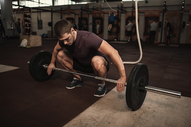 Athlète masculin musclé faisant deadlift avec haltères lourds à cross fit gym