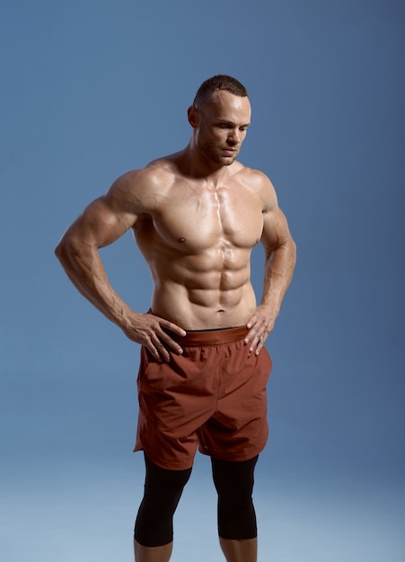 Athlète masculin musclé, séance photo en studio, fond bleu. Un homme avec une carrure athlétique, un sportif torse nu en vêtements de sport, un mode de vie sain et actif