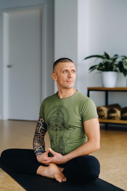 Un athlète masculin portant un t-shirt vert est assis dans la salle de sport avant une séance d'entraînement de yoga