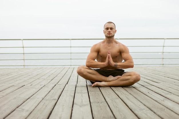 Un athlète musclé avec un torse nu médite sur la plage. Pratiquer le yoga hatha