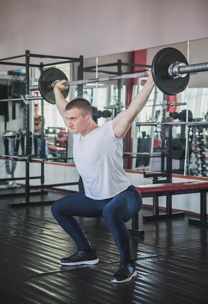 un athlète en pantalon de survêtement tient une barre au-dessus de sa tête au club de remise en forme