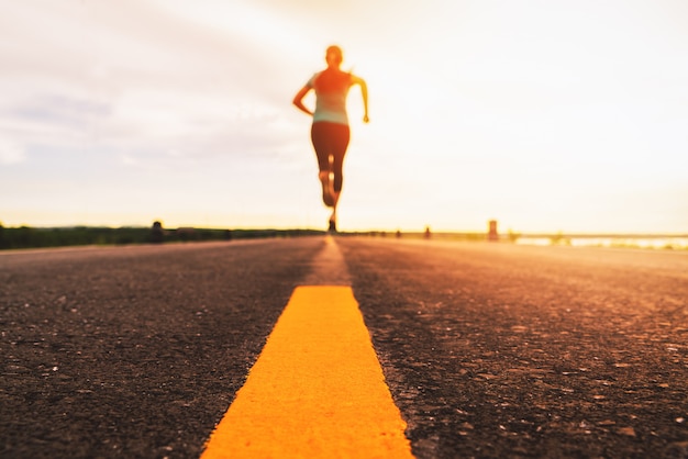 Athlète qui court sur le sentier de la route au coucher du soleil pour s'entraîner au marathon et au fitness. flou de mouvement de femme exerçant à l'extérieur