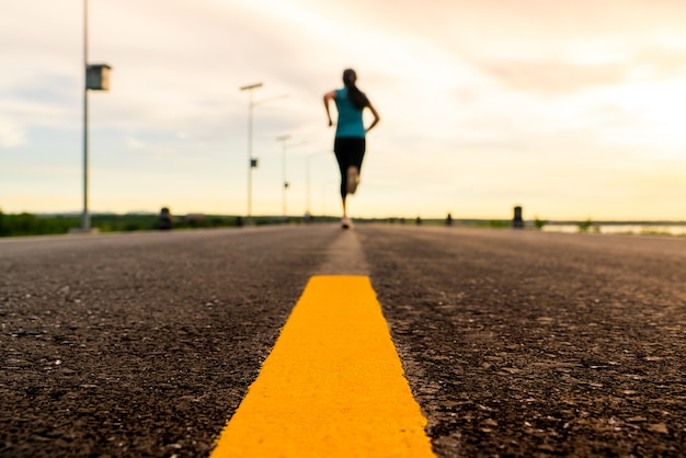 Athlète qui court sur le sentier routier au coucher du soleil pour le marathon et la remise en forme.