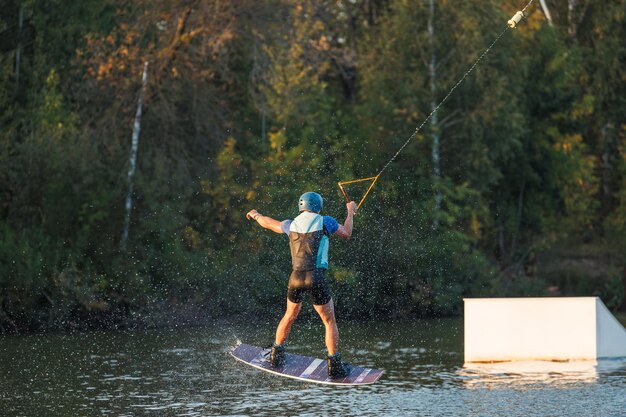 Un athlète saute par-dessus le parc aquatique Wakeboard au coucher du soleil. Le cavalier exécute un tour sur la planche