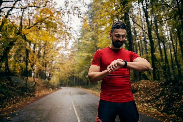 Un athlète se tient sur un temps pluvieux dans la nature et regarde la réalisation sur une montre intelligente