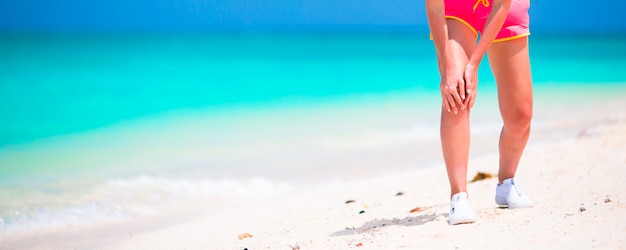 Athlète souffrant de douleurs à la jambe pendant l'exercice sur une plage de sable blanc