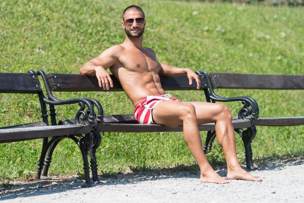 Athlète souriant avec torse nu assis et reposant sur un banc