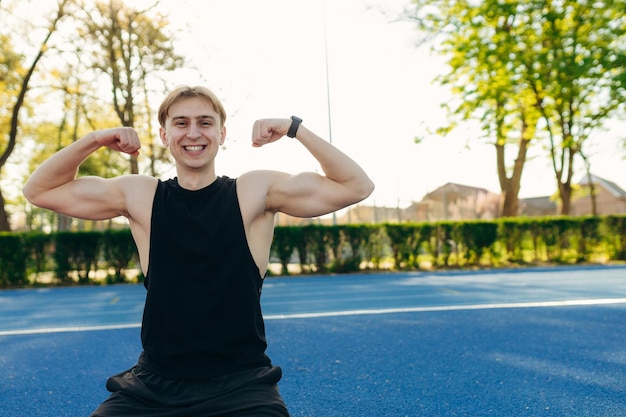 Athlète de succès sportif dans le stade homme heureux montre ses muscles triceps et biceps dans l'entraînement de gars de sport musclé du stade