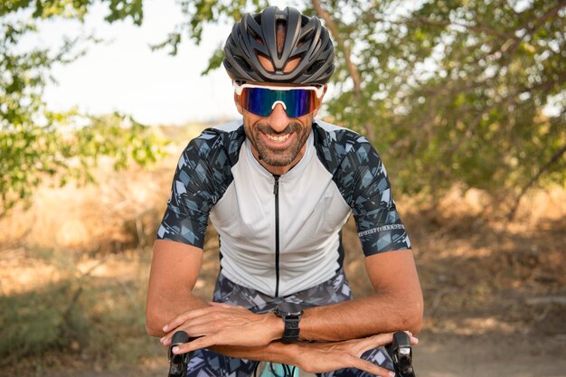 Athlète de triathlon appuyé sur le guidon souriant avec casque et lunettes de soleil. Sécurité