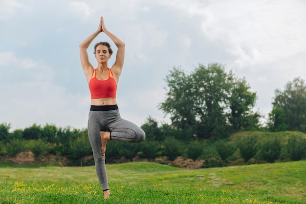 Athlétique belle femme fermant les yeux et respirant lentement tout en faisant du yoga en plein air