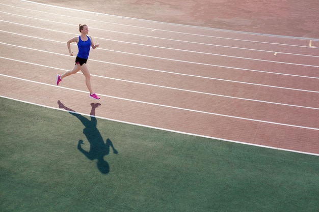 Athlétique jeune femme en baskets roses courir sur le stade de piste de course