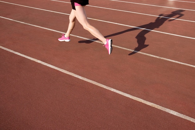 Athlétique jeune femme en baskets roses courir sur le stade de piste de course