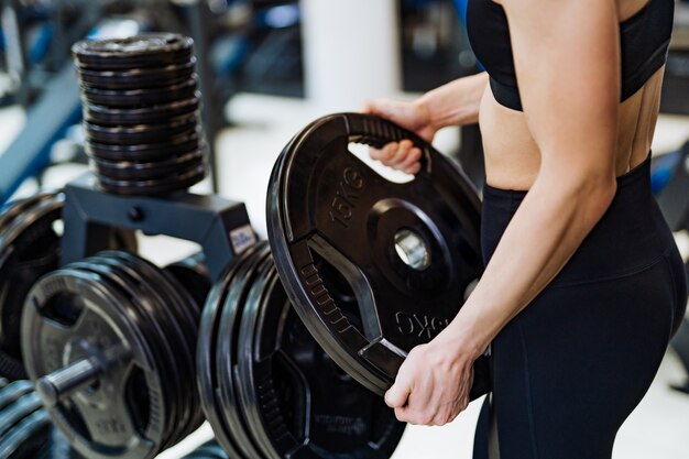 Athlétique jeune femme tenant un disque de barbell et exerçant dans la salle de gym.