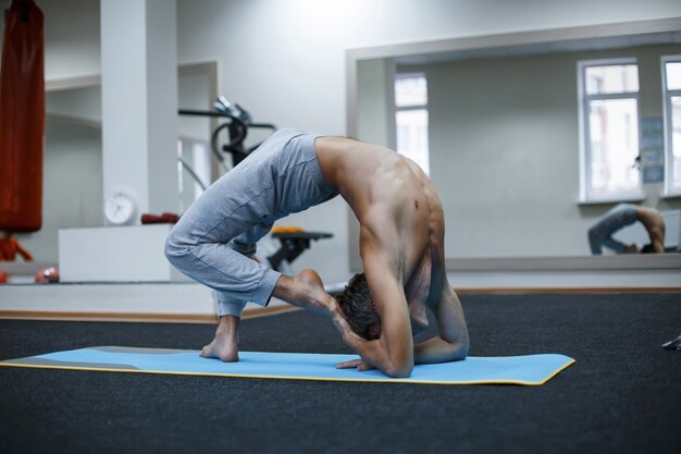 Athlétique jeune homme musclé travaillant, yoga, pilates, entraînement de remise en forme, faire un virage latéral, asana Parighasana, Gate Yoga Pose in gym