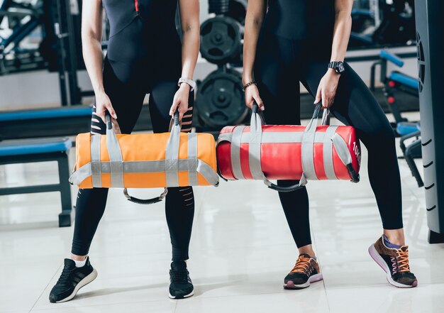 Athlétique jeunes femmes s'entraînant avec des sacs de sable sur fond gris. Centre Crossfit