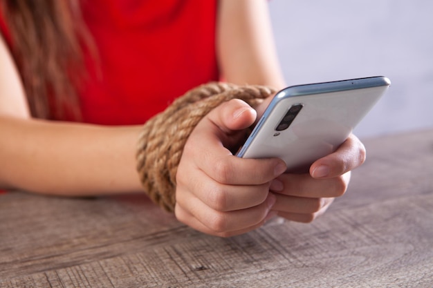 Attaché avec une corde, les mains des femmes tiennent le téléphone