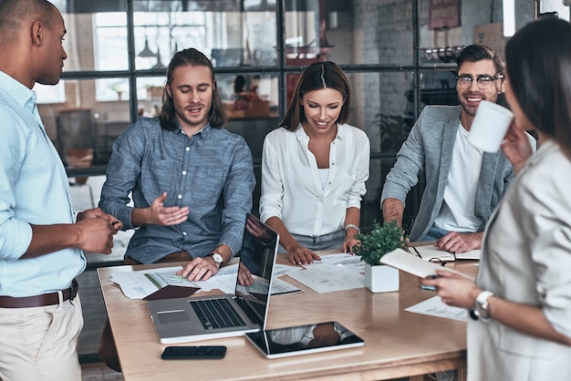 Atteindre les meilleurs résultats ensemble. Groupe de jeunes gens d'affaires communiquant et souriant tout en travaillant au bureau