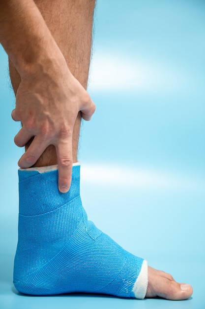 Attelle de cheville bleue. Jambe bandée moulée sur un patient de sexe masculin sur fond flou bleu clair. Concept de blessure sportive.