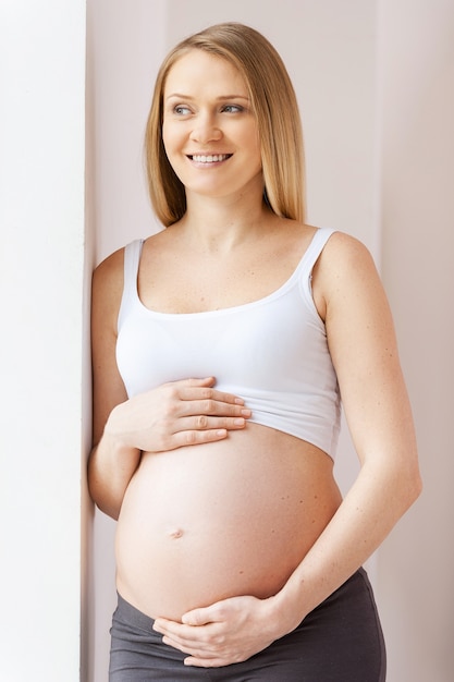 En attendant un bébé. Heureuse femme enceinte se penchant contre le mur et détournant les yeux