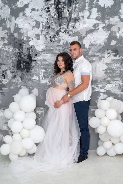 En attendant. Heureuse paire enceinte en vêtements de mode qui pose en studio