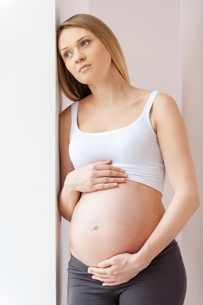 Attendre un bébé. Femme enceinte réfléchie se penchant au mur et regardant loin