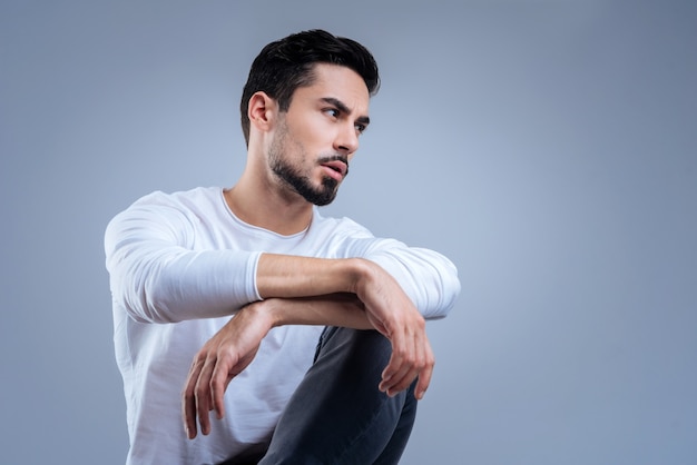 Attente. Sérieux jeune homme calme assis, les bras croisés et regardant au loin