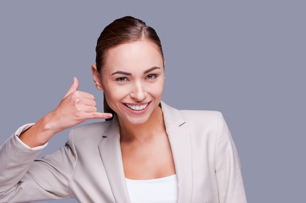 En attente de votre appel ! Cheerful young businesswoman gestes signe de téléphone et souriant