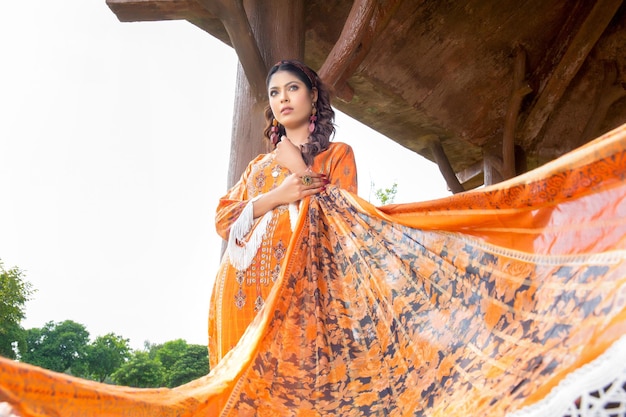 Attitude Desi Girl Landscape Holding Dupatta vêtue d'une robe Desi orange pour une séance photo