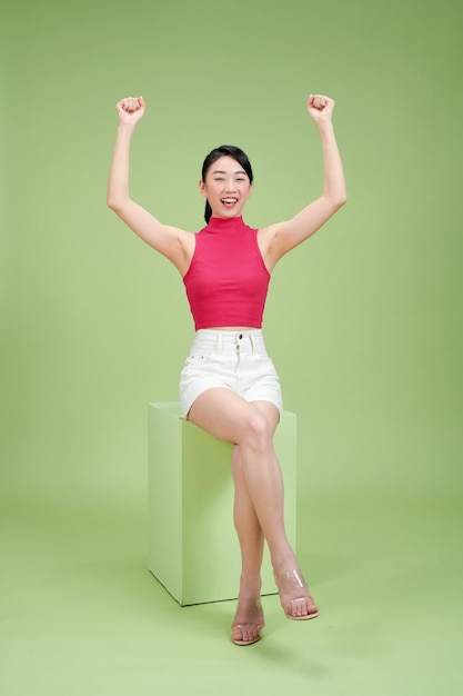 Attractive belle femme asiatique assise sur le podium et les mains en l'air les bras levés de bonheur