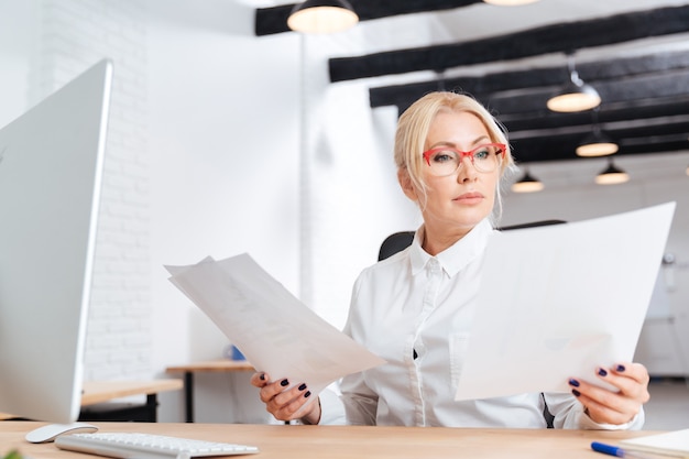 Attractive businesswoman mature pensive lisant des papiers au bureau