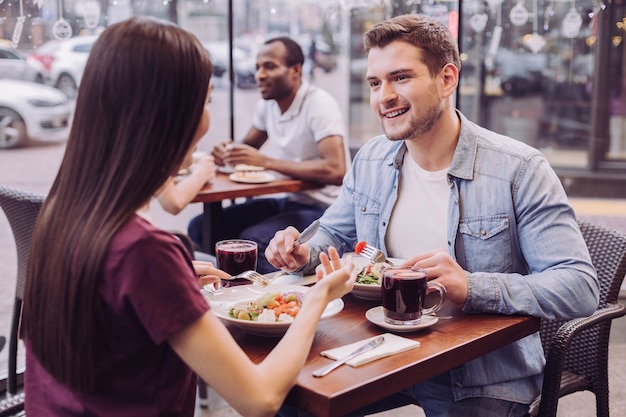 Attractive couple énergique communiquant et posant au café tout en bel homme souriant