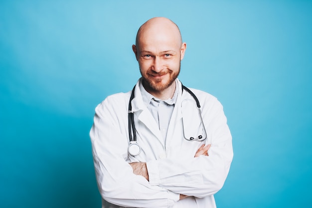 Attractive sympathique barbu chauve souriant médecin regardant la caméra isolé sur fond bleu