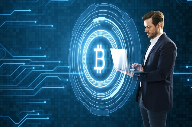 Attractive young european businessman using laptop with creative glowing crypto coins on dark blue background with circuit lines Cryptocurrency digital money technology and economic network concept