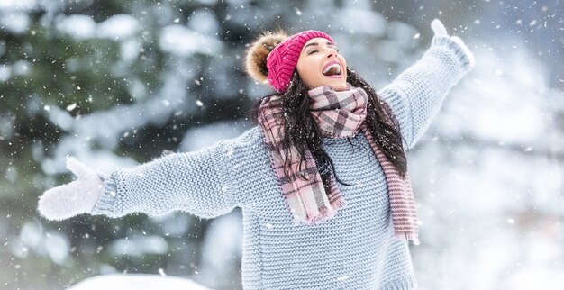 Attraper des flocons de neige pour ouvrir la bouche à l'extérieur par une femme heureuse en pull, écharpes et chapeau d'hiver.