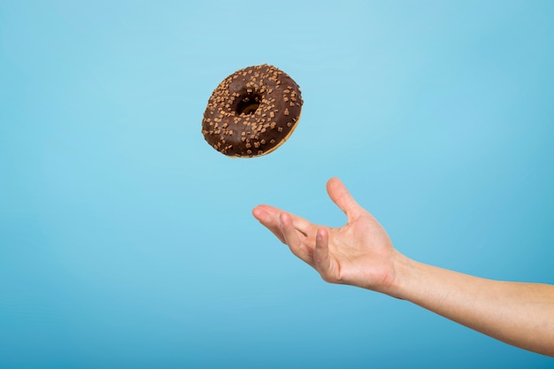 Attraper à la main un beignet avec du glaçage au chocolat. Concept de cuisson, fait à la main. Mise à plat, vue de dessus