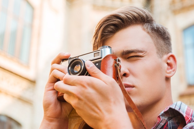 Attraper un moment. Low angle view of beau jeune homme photographiant avec son appareil photo vintage tout en se tenant à l'extérieur