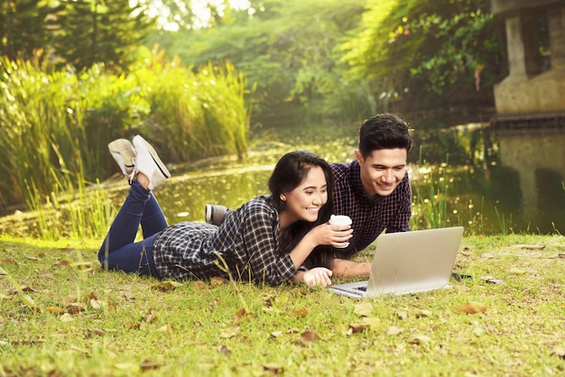 Attrayant couple asiatique, regarder des films sur un ordinateur portable en position couchée sur l&#39;herbe verte