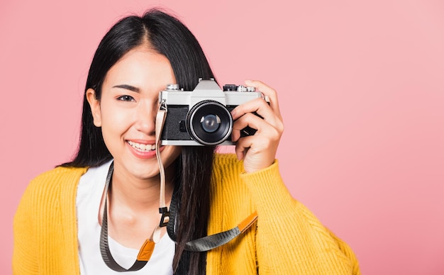 Attrayant énergique portrait asiatique heureux belle jeune femme photographe souriant prenant une photo et regardant le viseur sur un appareil photo rétro vintage prêt à tirer isolé sur fond rose