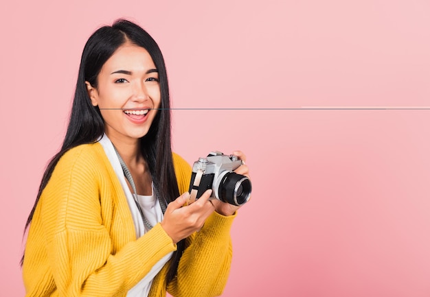 Attrayant énergique portrait asiatique heureux belle jolie jeune femme adolescente excitée souriante tenant un appareil photo vintage, prise de vue en studio isolée sur fond rose, photographe voyageuse