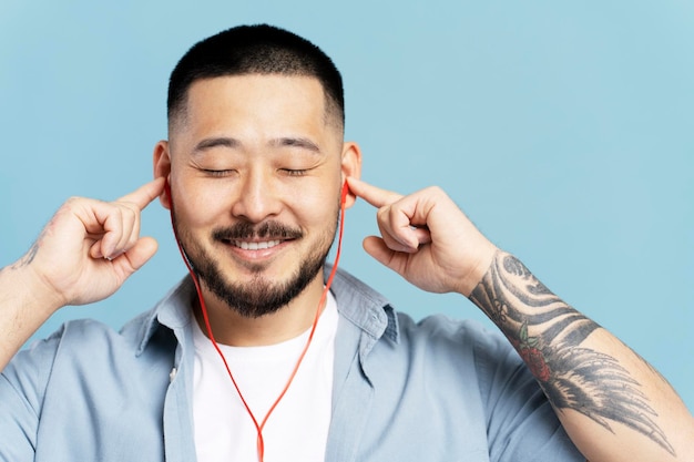 Attrayant homme coréen écoutant de la musique dans un casque les yeux fermés isolé sur fond bleu